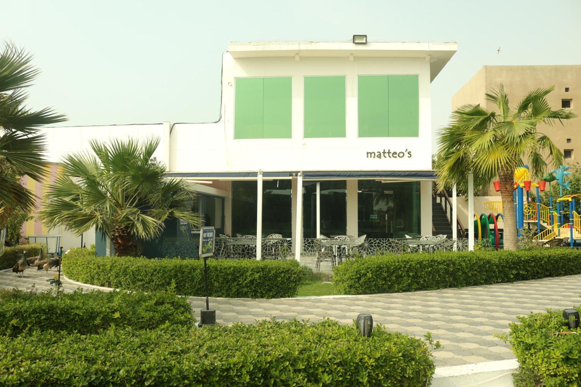 Lagoona Beach Luxury Resort And Spa Manama Luaran gambar The photo shows a building with the name "matteo's" displayed prominently on the front. The structure features large windows and green shutters. There is a landscaped area in front with bushes and palm trees, along with a paved pathway leading up to 