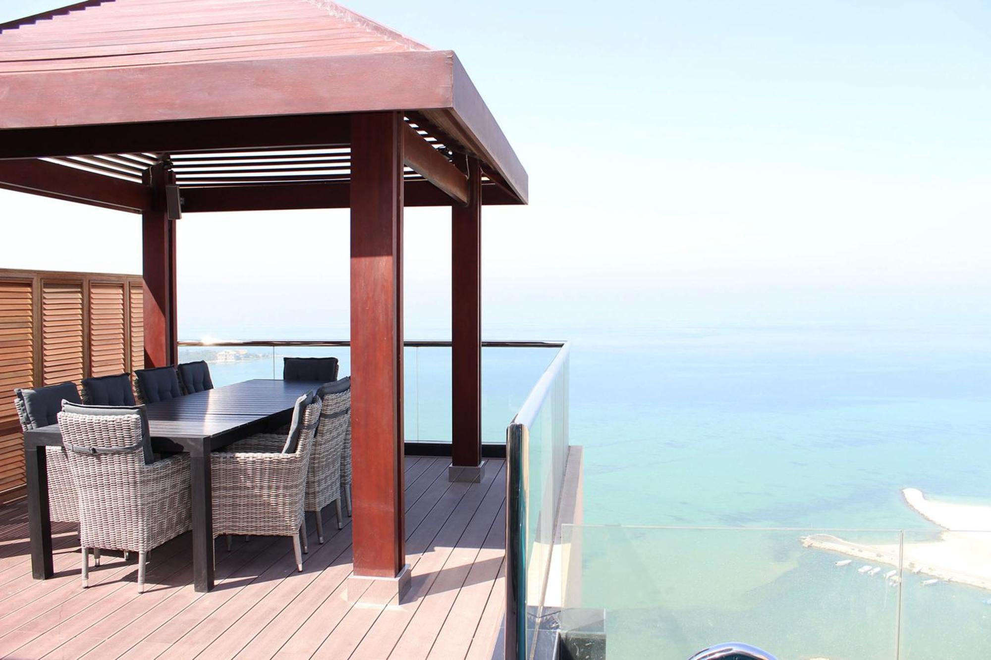 Lagoona Beach Luxury Resort And Spa Manama Luaran gambar The photo showcases a stylish outdoor patio or terrace area. It features a wooden structure with a sloped roof, providing a shaded space. There is a large table made of dark wood, surrounded by several wicker chairs. The patio is elevated and has gla