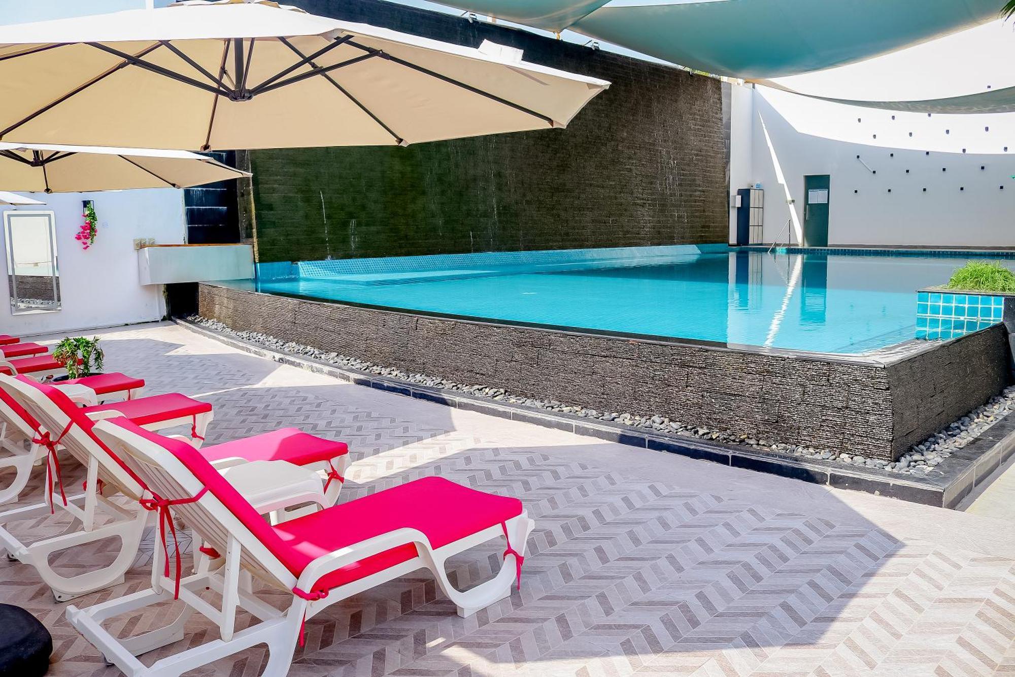 Lagoona Beach Luxury Resort And Spa Manama Luaran gambar The photo shows a pool area featuring a rectangular swimming pool with clear blue water. Surrounding the pool are light-colored lounge chairs with pink cushions, positioned under large umbrellas for shade. The pool is bordered by a textured wall, and