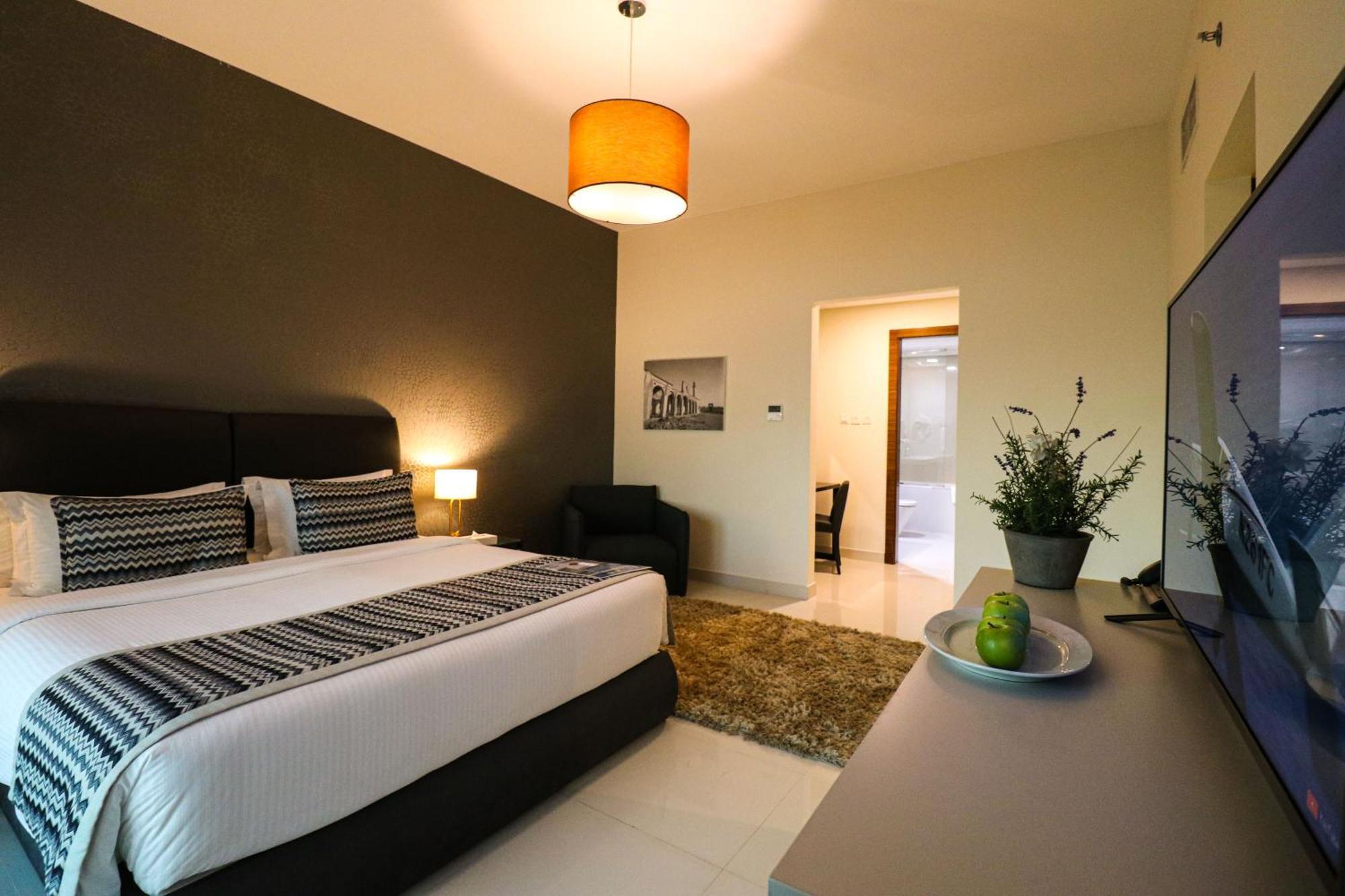 Lagoona Beach Luxury Resort And Spa Manama Luaran gambar The photo shows a modern hotel room. It features a large bed with a neatly made white and dark-colored duvet. On either side of the bed, there are bedside tables with lamps. The wall behind the bed is painted in a dark color, creating a contrast with