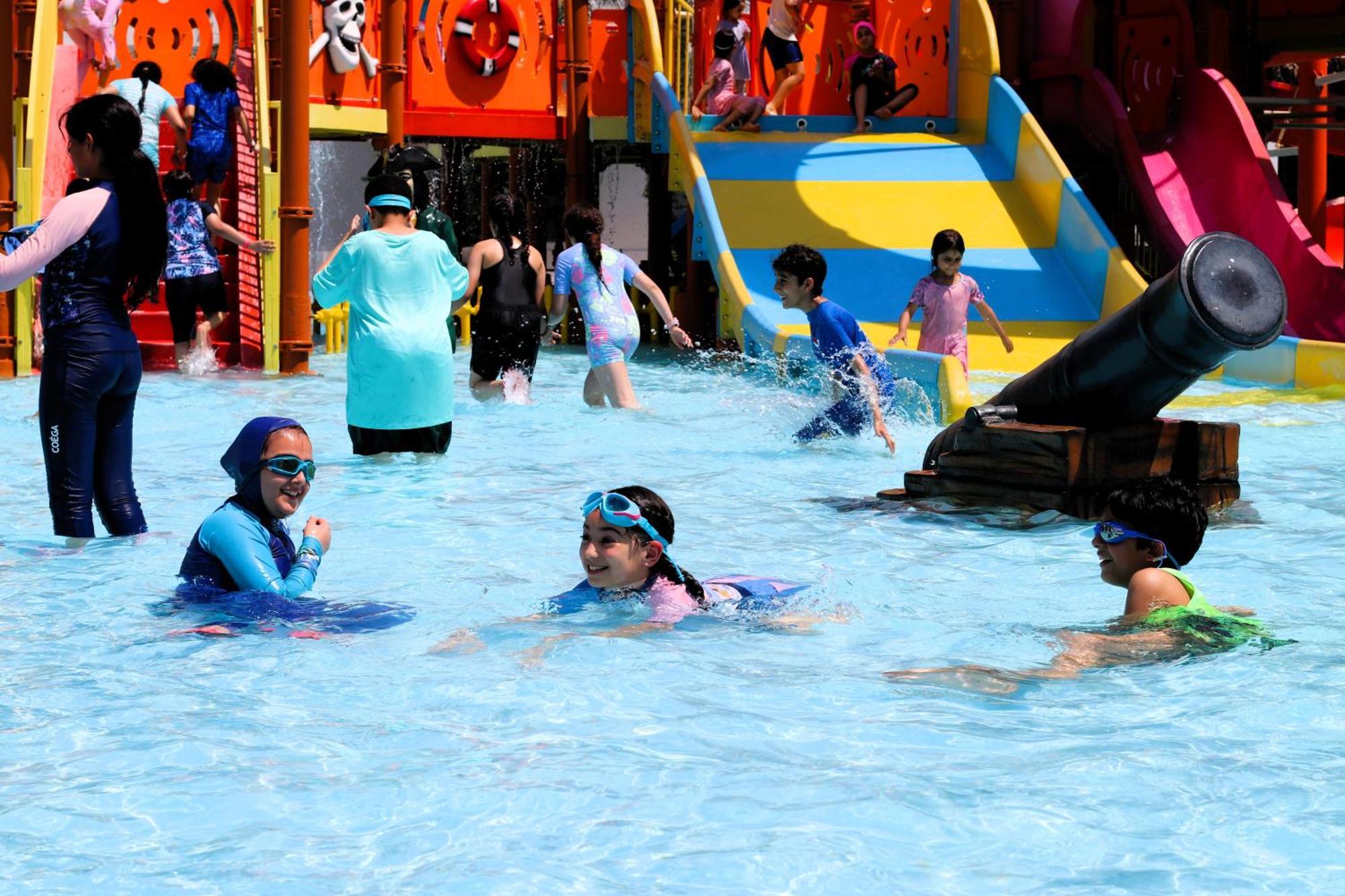 Lagoona Beach Luxury Resort And Spa Manama Luaran gambar The photo shows a vibrant water park scene with several children playing in a shallow pool. Some are swimming and splashing around, while others are playing on colorful slides in the background. The atmosphere is lively and cheerful, with kids of var