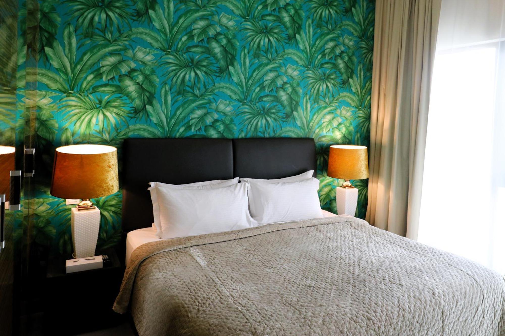 Lagoona Beach Luxury Resort And Spa Manama Luaran gambar The photo shows a stylish bedroom featuring a large bed with white pillows and a gray blanket. The headboard is upholstered in black, providing a modern touch. Behind the bed, there is a vibrant green wallpaper with a tropical leaf pattern, adding a 