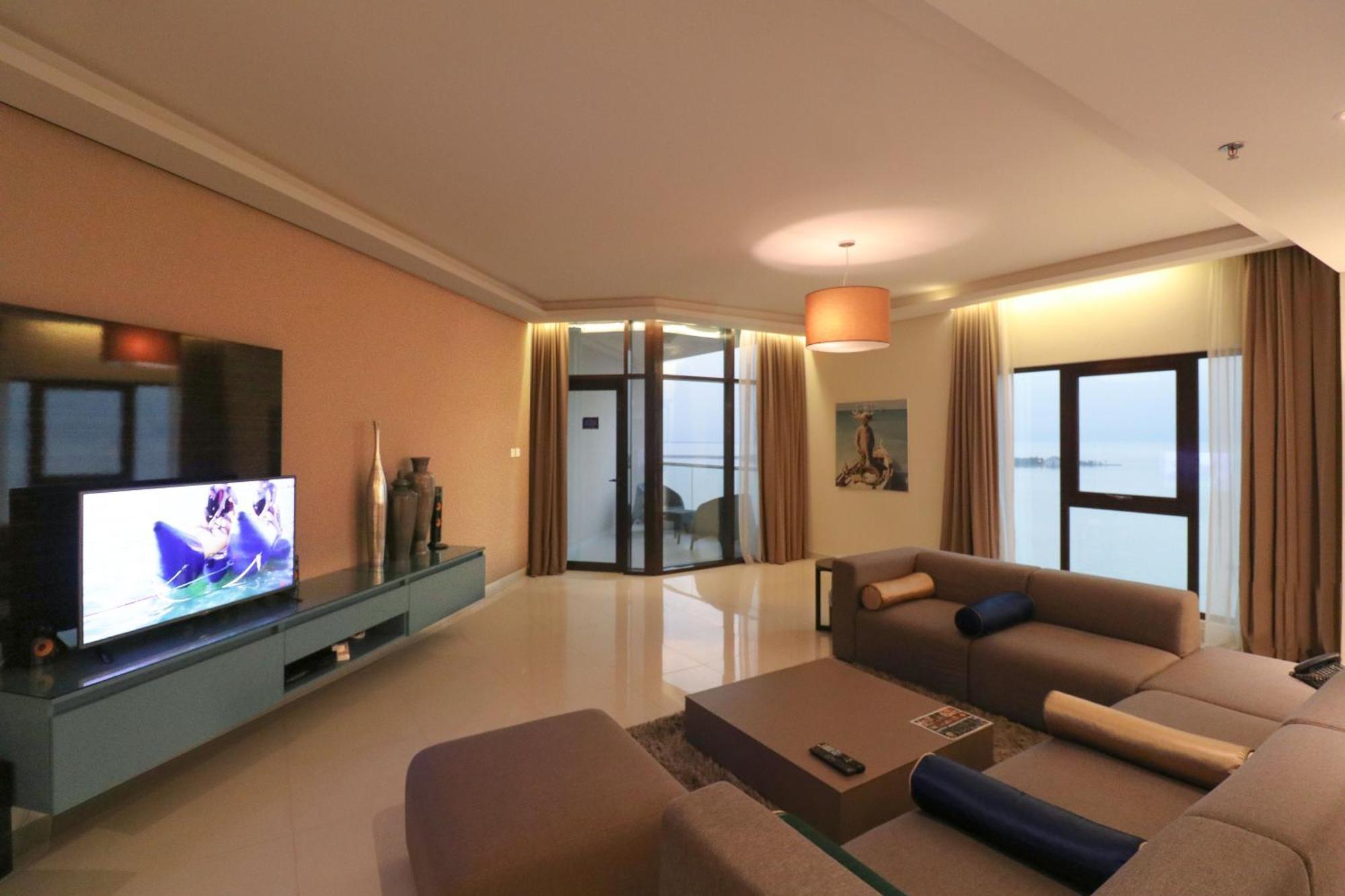 Lagoona Beach Luxury Resort And Spa Manama Luaran gambar The photo shows a modern living room with a sleek design. There is a large wall-mounted television on a contemporary entertainment unit, with decorative items placed beside it. The room features a comfortable sectional sofa in light tones, with a cof