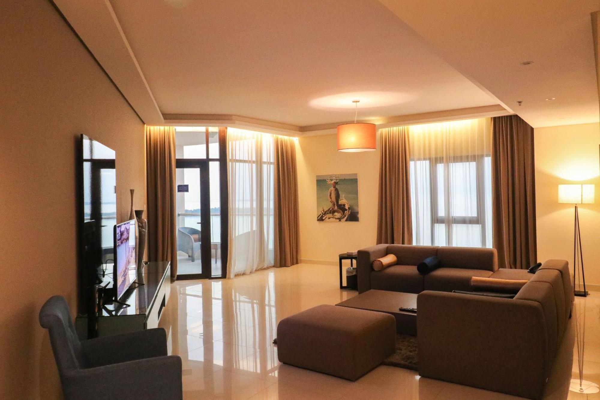 Lagoona Beach Luxury Resort And Spa Manama Luaran gambar The photo shows a modern living room with a spacious and elegant design. It features a large couch in neutral tones, a soft ottoman, and a stylish coffee table. The walls are painted in a light color, and there are large windows with sheer curtains a