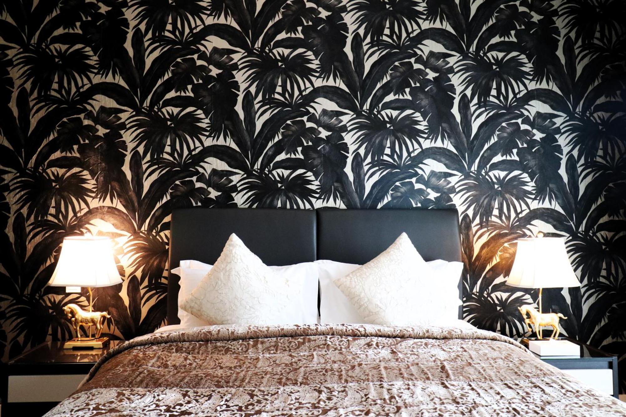 Lagoona Beach Luxury Resort And Spa Manama Luaran gambar The photo depicts a stylish bedroom featuring a distinctive wall covered in a black and white tropical foliage wallpaper. The bed has a modern black headboard and is adorned with white pillows, creating a clean and elegant look. A textured brown thro