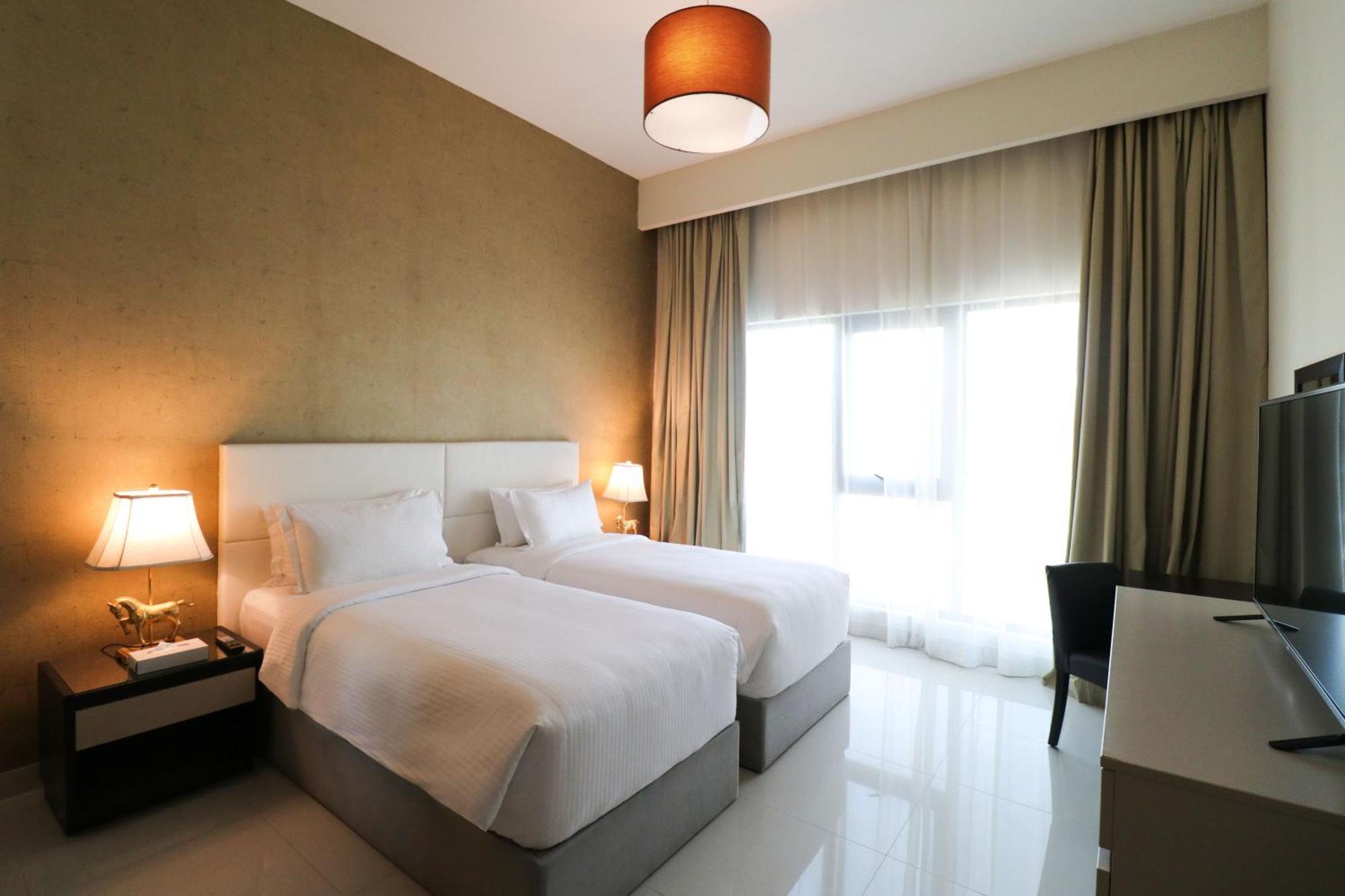 Lagoona Beach Luxury Resort And Spa Manama Luaran gambar The photo shows a hotel room featuring two single beds with white bedding. The walls have a neutral tone, and there's a large window covered by light, sheer curtains allowing natural light to enter. On either side of the beds, there are bedside table