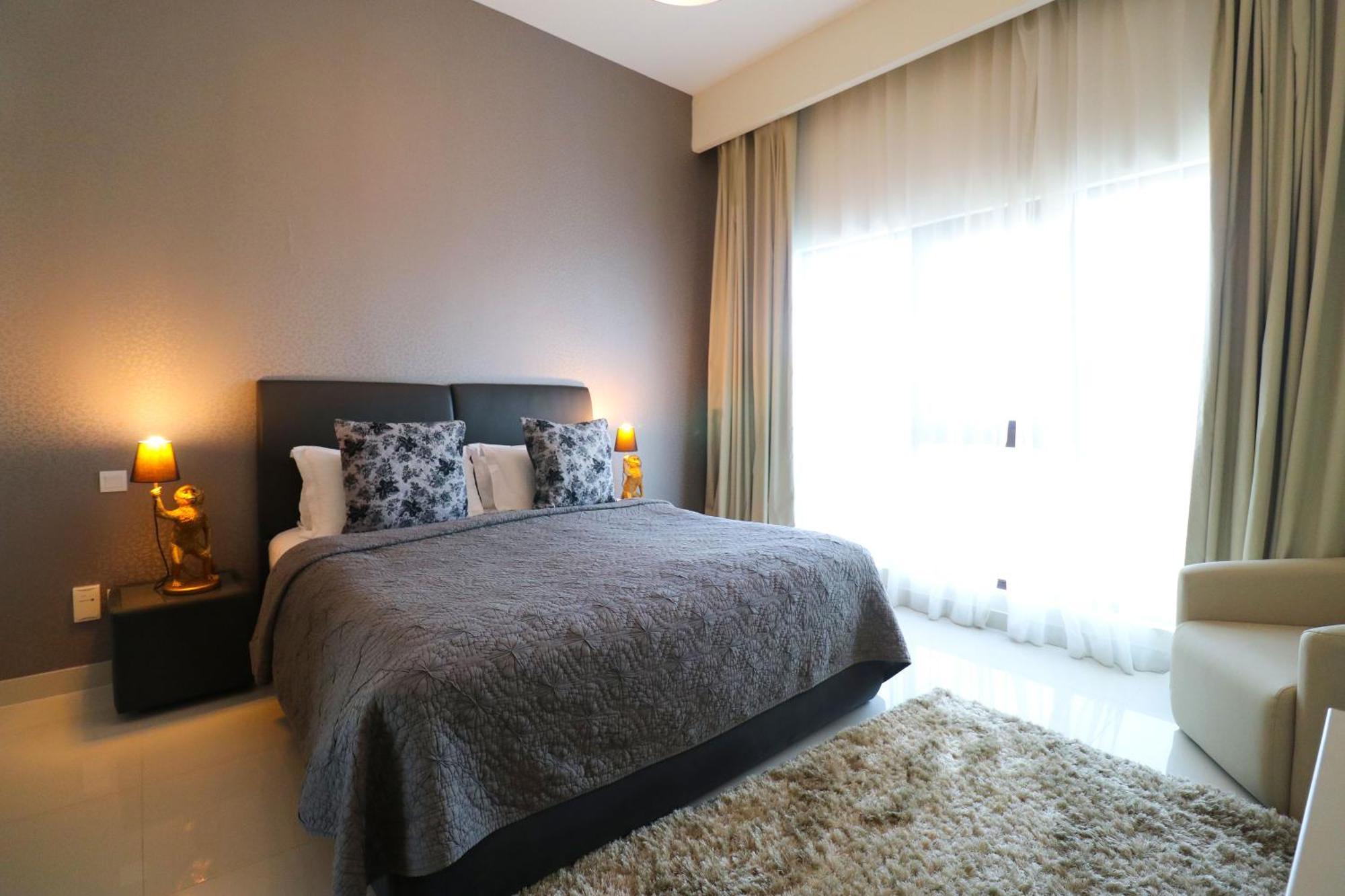 Lagoona Beach Luxury Resort And Spa Manama Luaran gambar The photo shows a stylish bedroom with a modern design. It features a large bed with a dark gray bedspread and decorative pillows. On either side of the bed are two wooden nightstands, each with a lamp. There is a large window covered with light, flo
